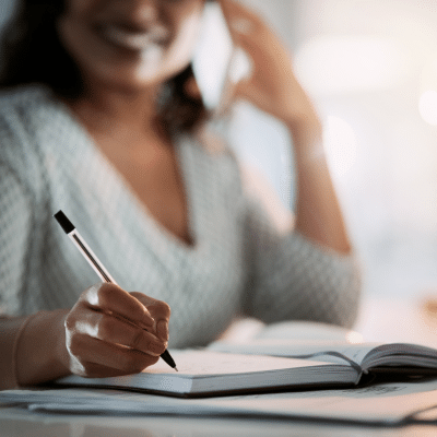 Smiling woman writing notes while on a phone call—taking action with a Capability Statement for Federal contracting