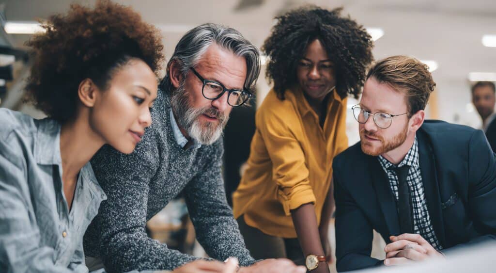 Diverse Federal business development team collaborating and reviewing insights during a Hot Wash meeting to improve performance and trust.